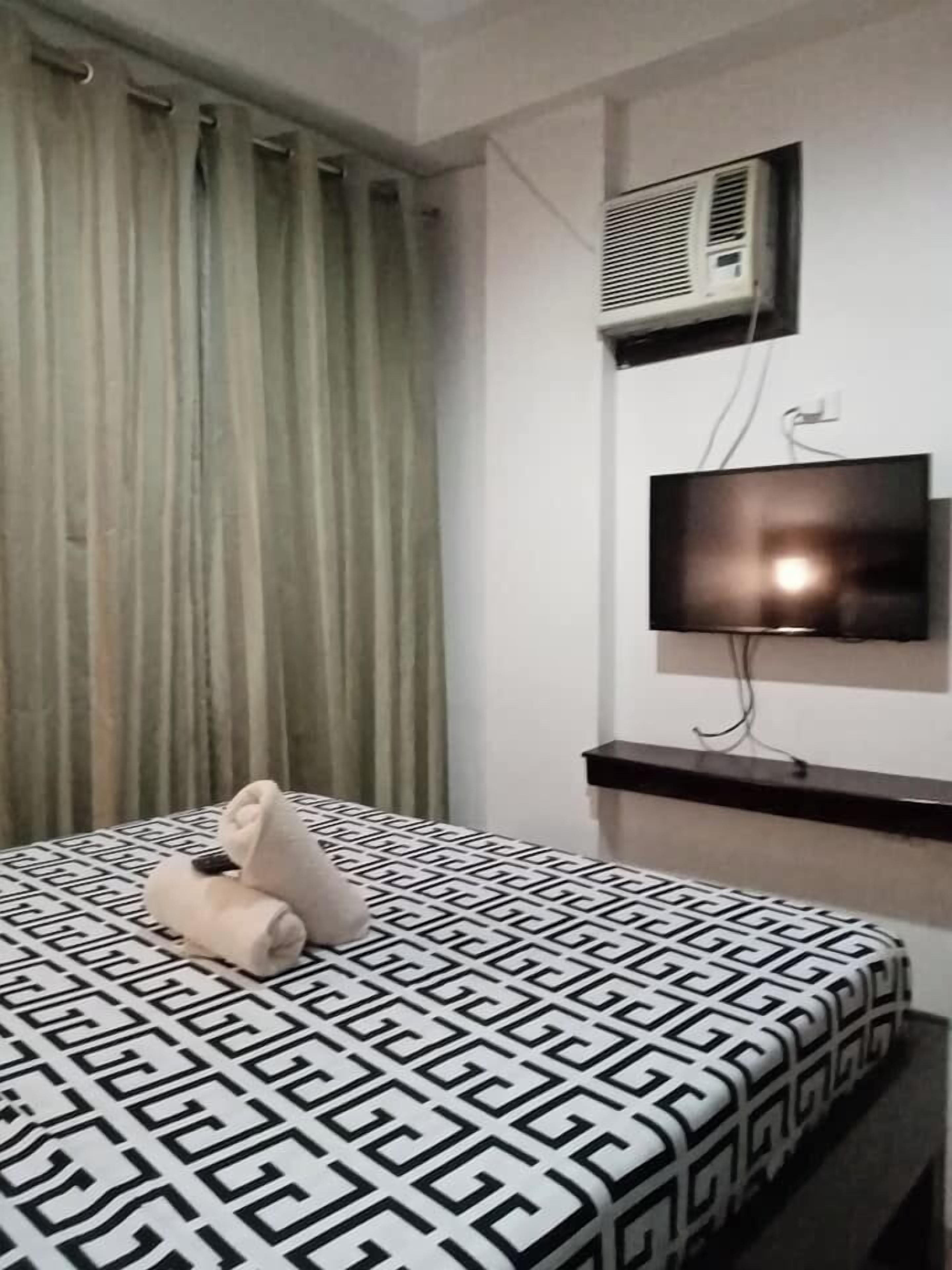A hotel room with a bed, a TV mounted on the wall, and an air conditioning unit.