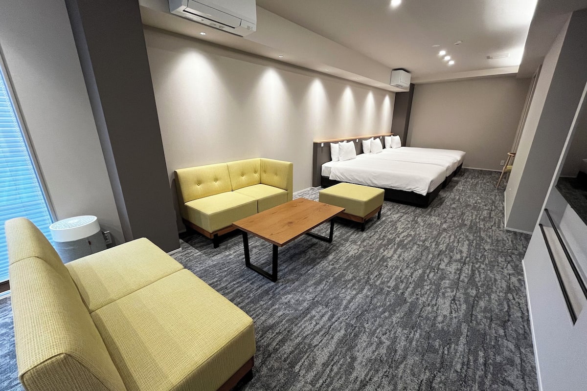 A hotel room with a bed, a sofa, a small table, and a window.