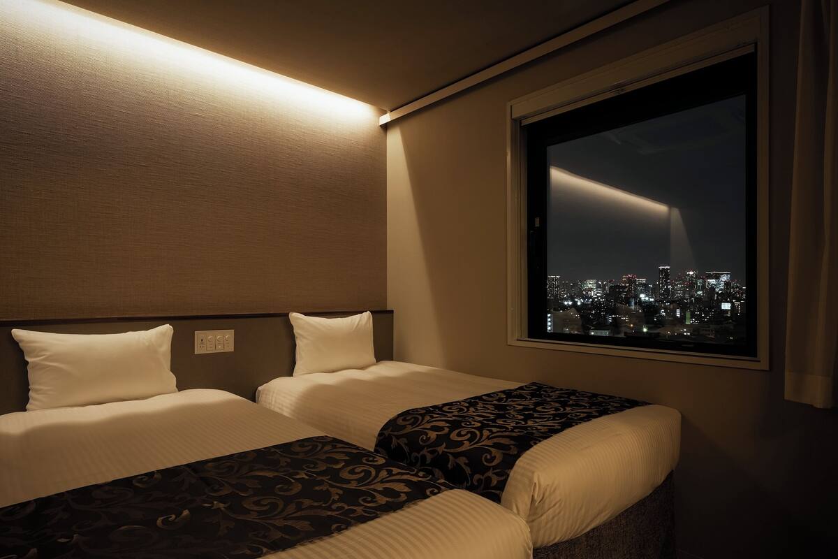 A hotel room with two beds, a city view, and a large window.