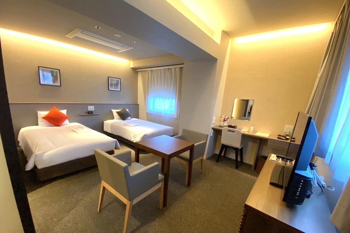 A hotel room with two beds, a desk, a chair, a television, and a window with curtains.