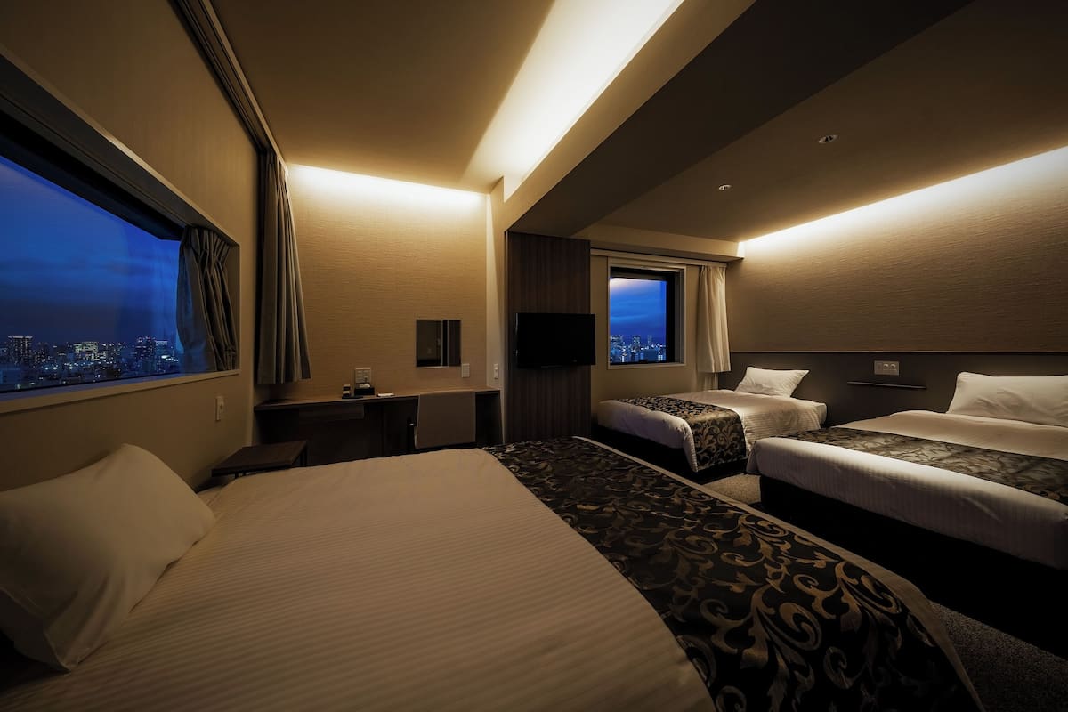 A hotel room with a large bed, two smaller beds, a desk, a TV, and a city view.