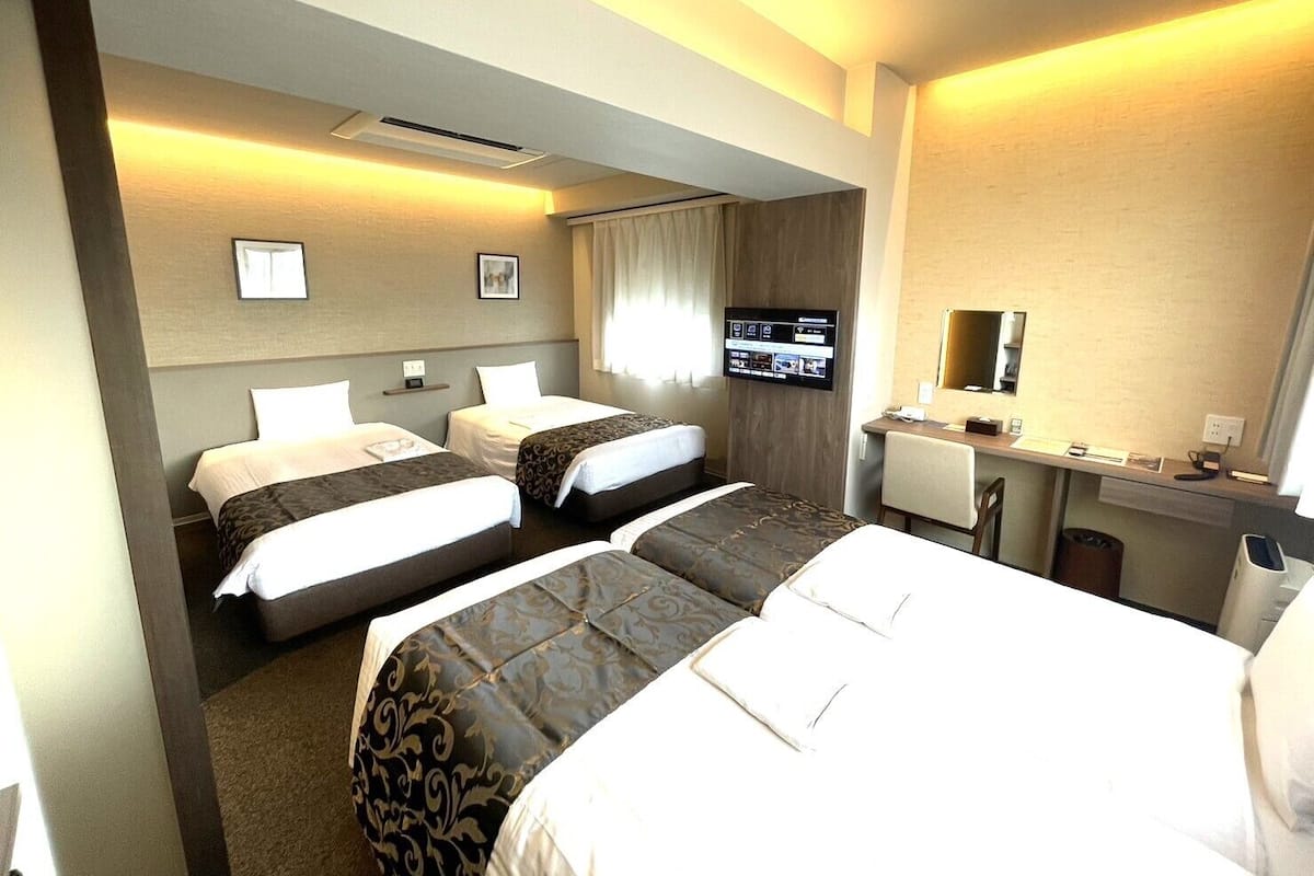 A hotel room with two beds, a desk with a chair, a television, and a mirror.