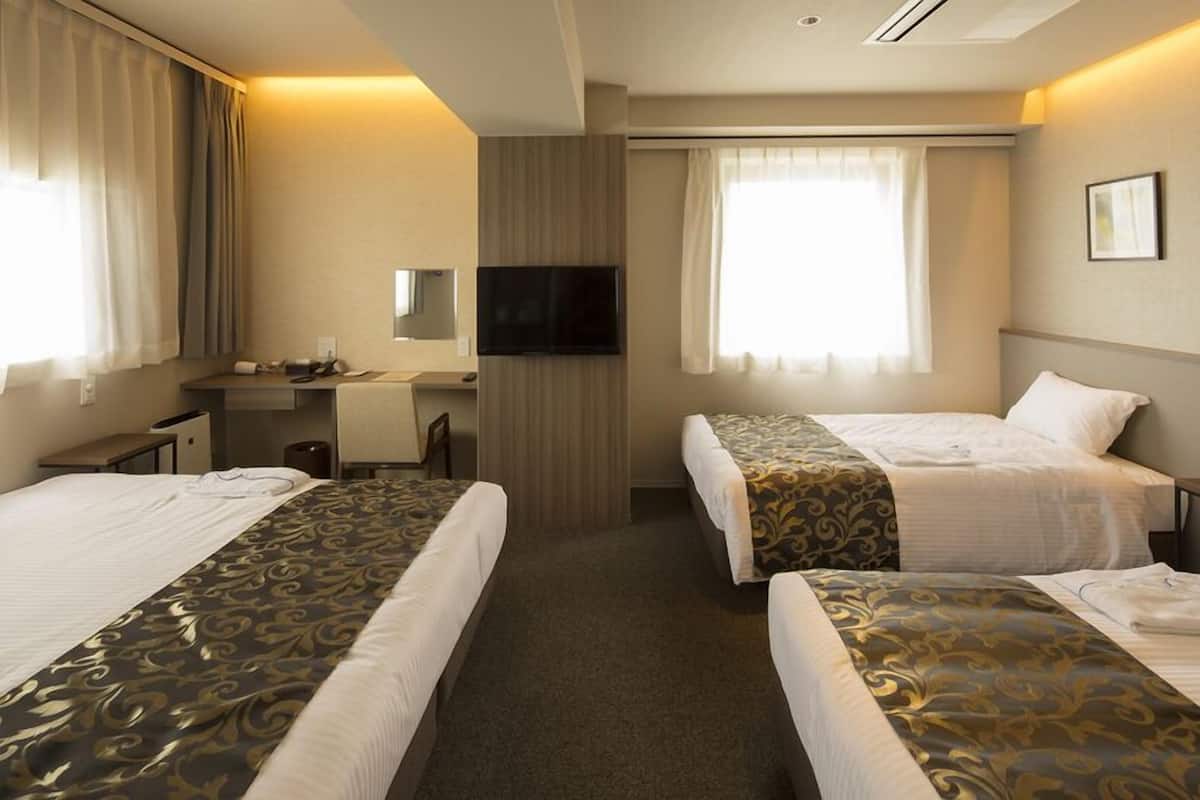 A hotel room with two beds, a desk, a chair, a television, and a window with curtains.