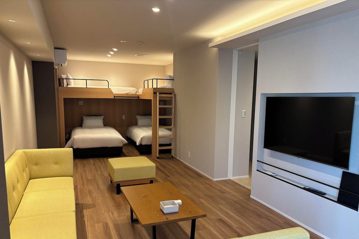 A hotel room with a sofa, two beds, a TV, and a wooden table.