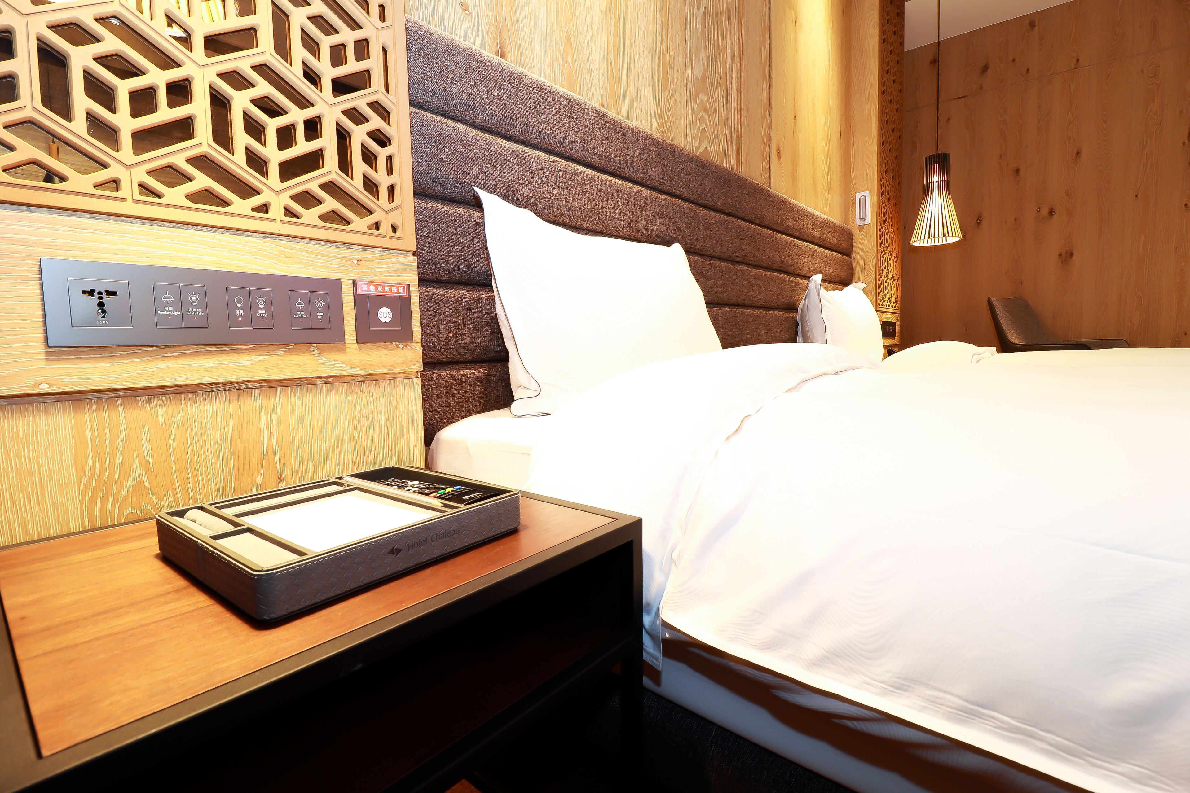 A hotel room with a wooden headboard, a control panel on the nightstand, and a bed with white bedding.