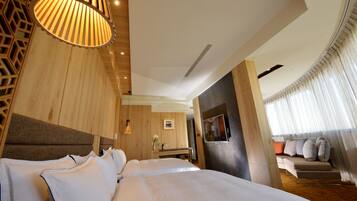 Una habitación de hotel moderna con una cama grande, cabecera de madera, televisión y una zona de estar con sofá y cortinas.