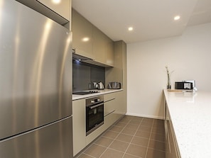 A modern kitchen with stainless steel appliances, a built-in oven, and a microwave on the countertop. - Accommodate Canberra - Quayside (Kingston)