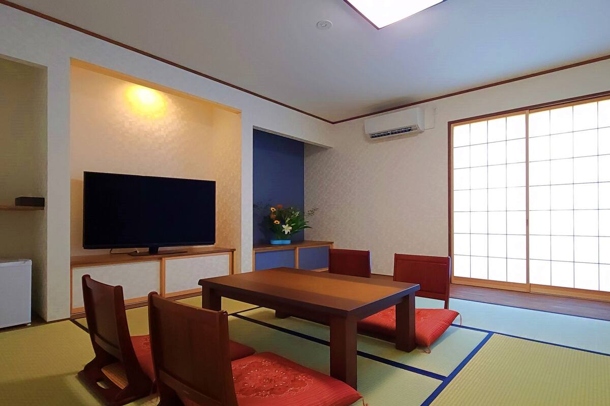 Perinteinen japanilaistyylinen huone, jossa on tatamimatto, matala pöytä ja punaiset tyynyt.