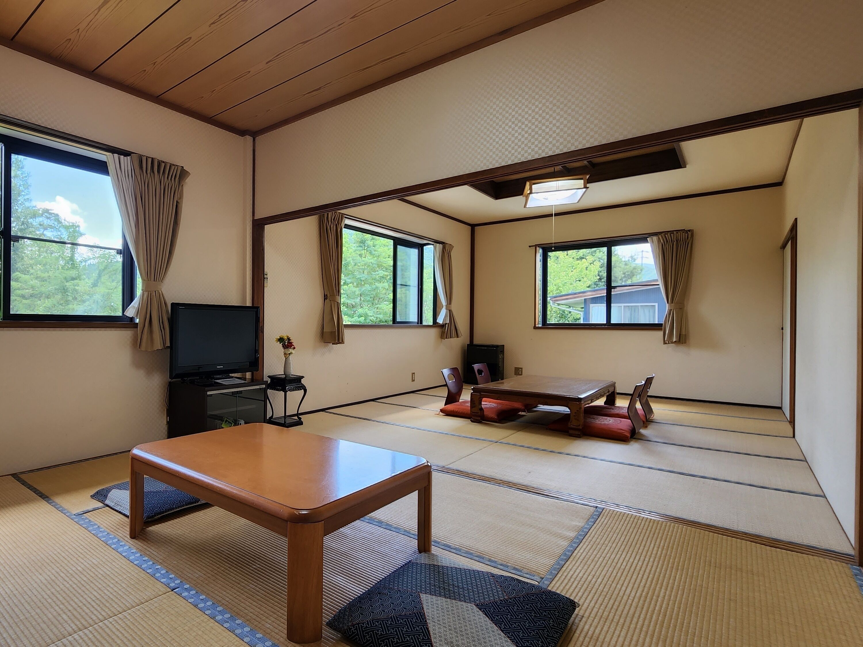 Una habitación tradicional japonesa con suelo de tatami, una mesa de madera, un televisor y un escritorio con un jarrón.