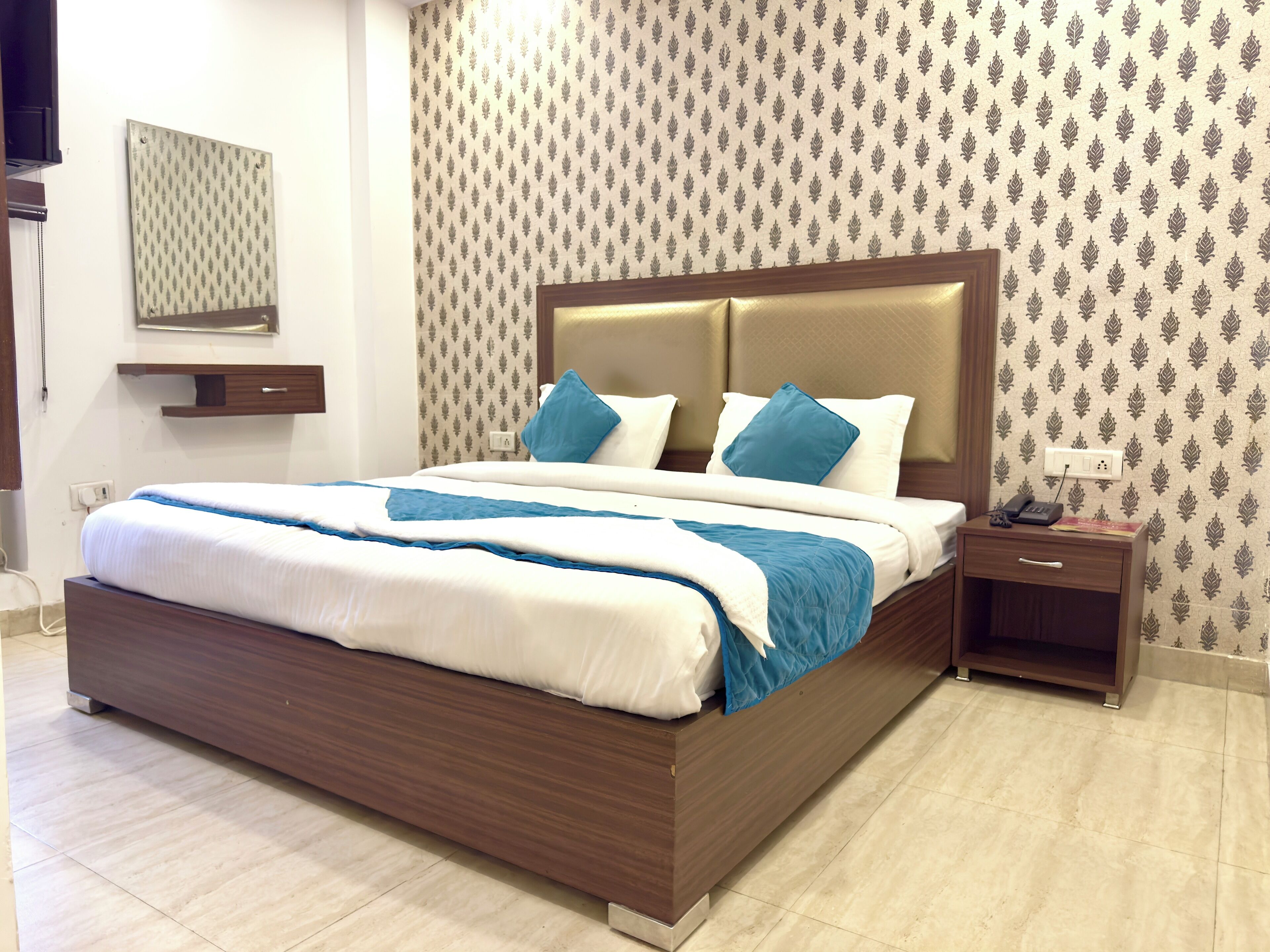 A neatly made bed with a wooden headboard, a bedside table with a lamp, and a patterned wallpaper.