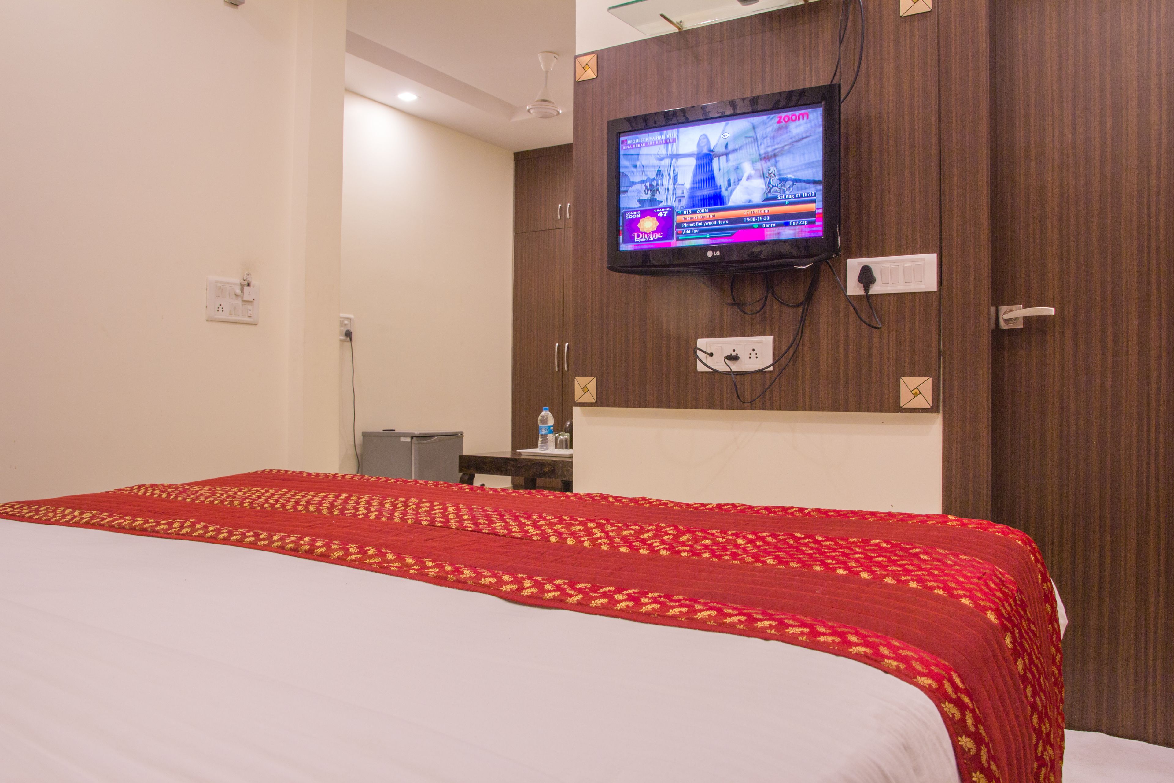 A hotel room with a large bed, a flat-screen TV mounted on the wall, and a desk with a chair.