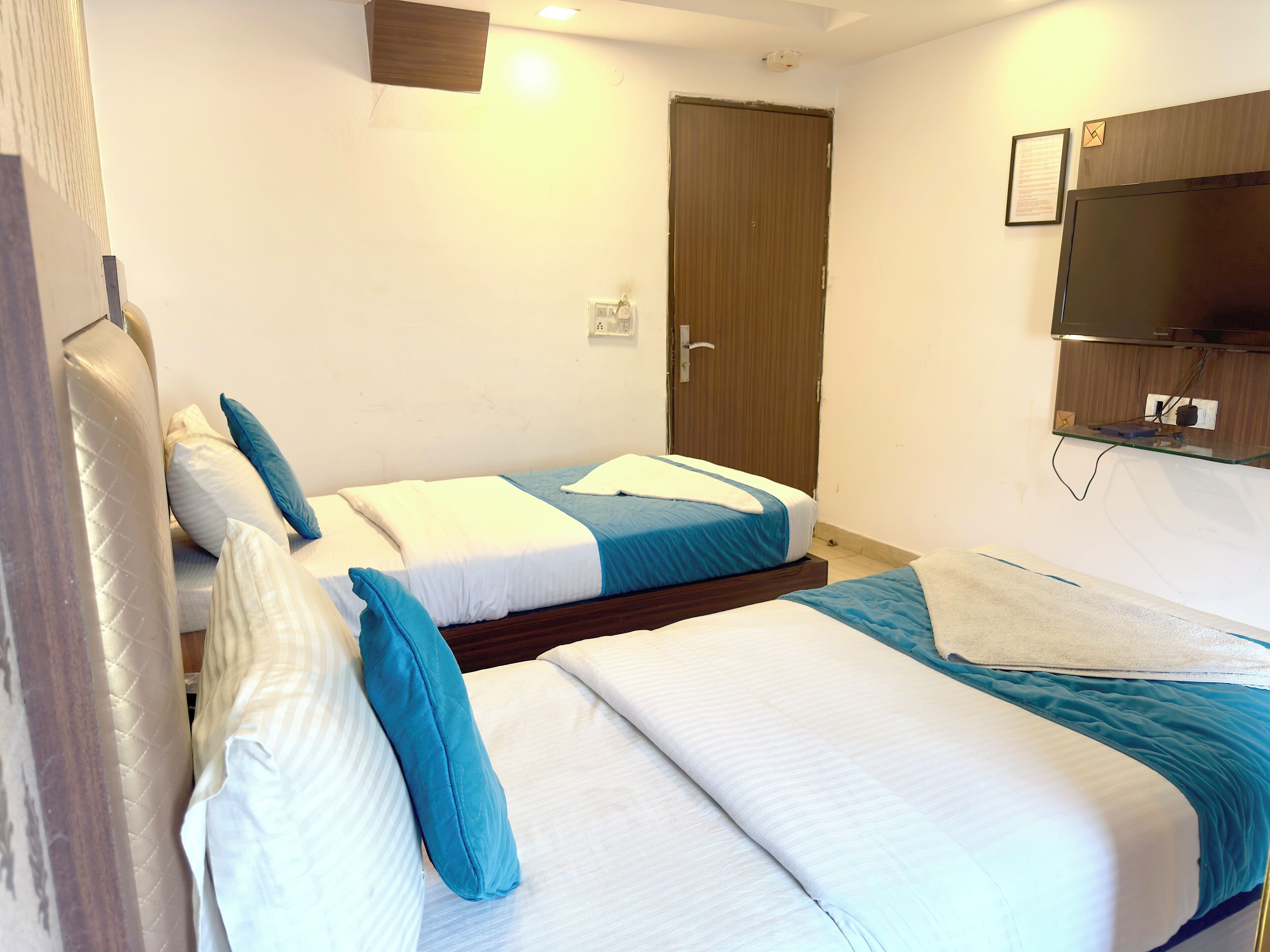 A hotel room with two beds, a wooden door, a mounted television, and a small desk with a chair.