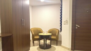 A room with a wooden wardrobe, two armchairs, a small round table, and a door with a handle. - Hotel Pawan Plaza - Near BLK and Ganga Ram Hospital - Karol Bagh (New Delhi)