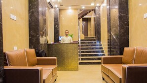 A hotel lobby with a reception desk, two leather sofas, a staircase, and a marble wall. - Hotel Pawan Plaza - Near BLK and Ganga Ram Hospital - Karol Bagh (New Delhi)