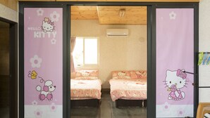 Una habitación con dos camas, cada una con cabecera temática de Hello Kitty. Hay una ventana con cortinas, un equipo de aire acondicionado en la pared y techo de madera.