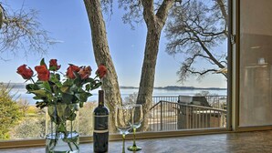 A table with a vase of red roses, a bottle of wine, and two wine glasses. The table is near a window with a view of trees and a body of water. - 'Casa d'Amore': Extravagant Lakefront Villa! (Granite Bay)