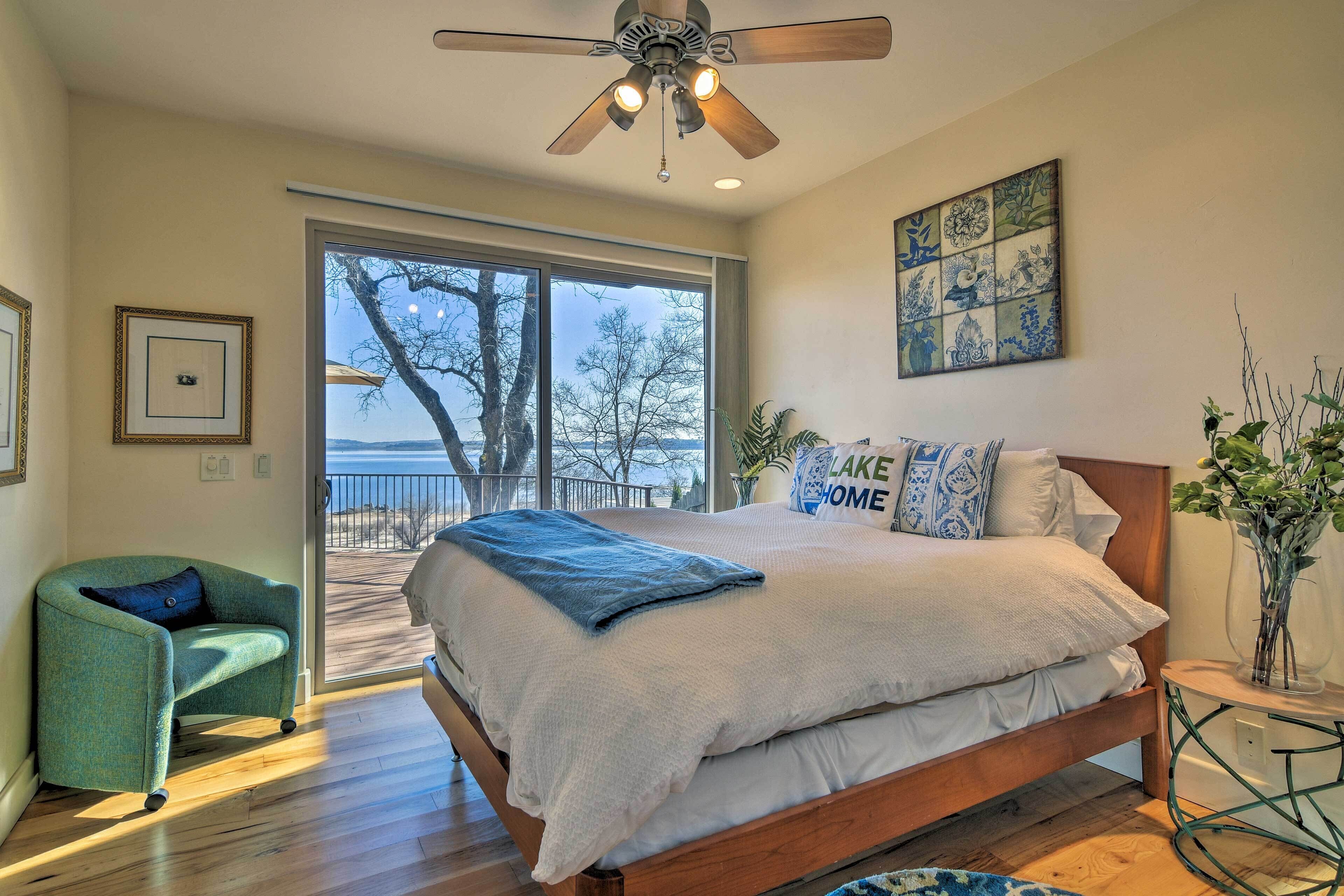 A bedroom with a large bed, a ceiling fan, a view through a sliding door to the outdoors, and a framed picture on the wall.