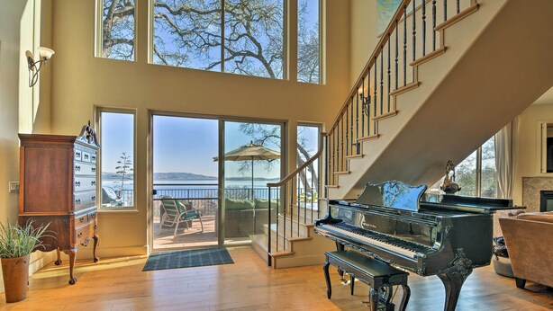 A spacious living room with a grand piano, large windows, a staircase, and a view of the outdoors. - 'Casa d'Amore': Extravagant Lakefront Villa! (Granite Bay)