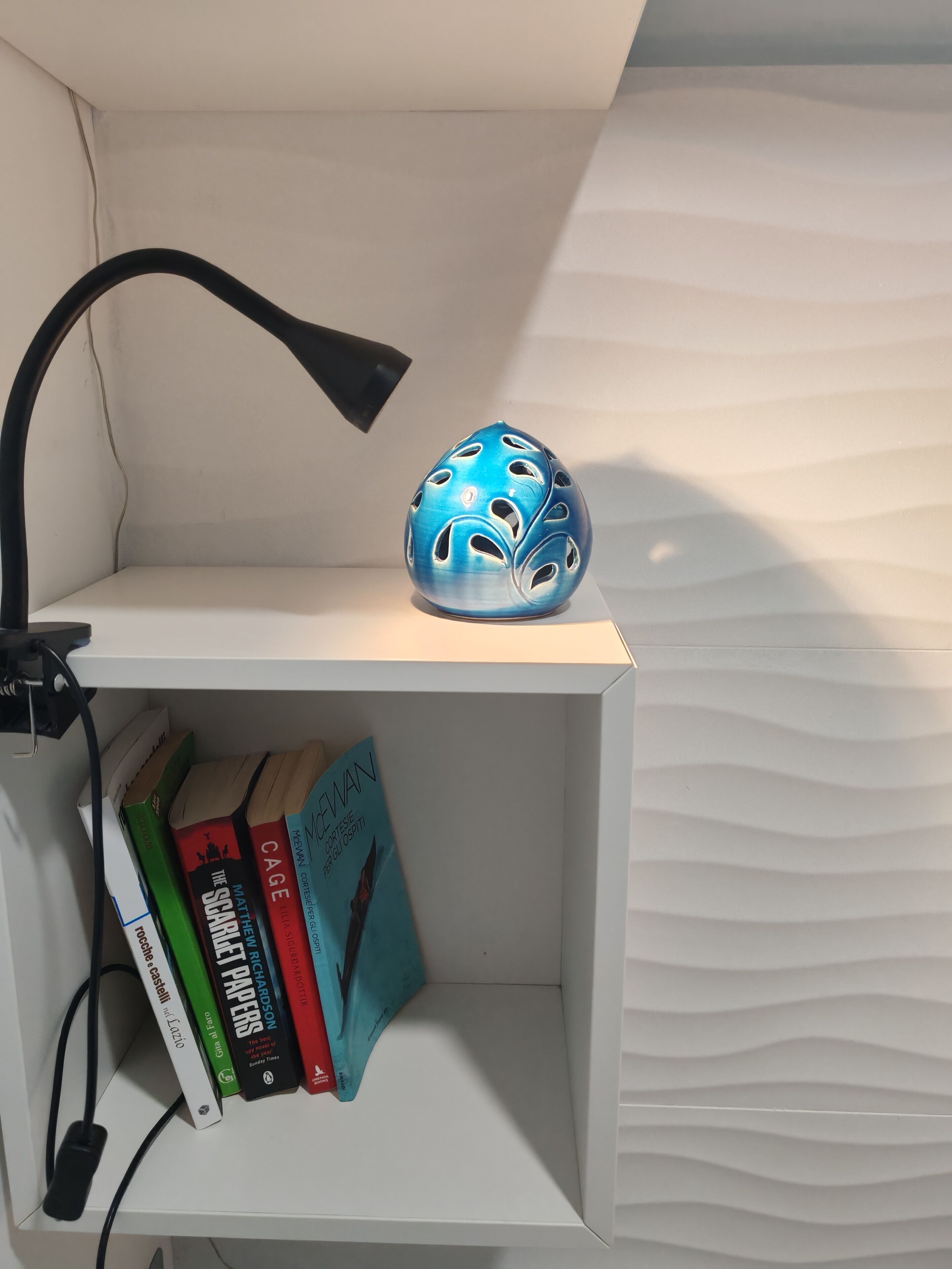 Ein weißes Regal mit einem blauen Keramikobjekt und Büchern.