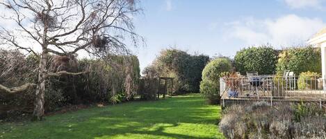 Un jardín bien cuidado con césped, un árbol y una zona vallada con mobiliario de exterior.