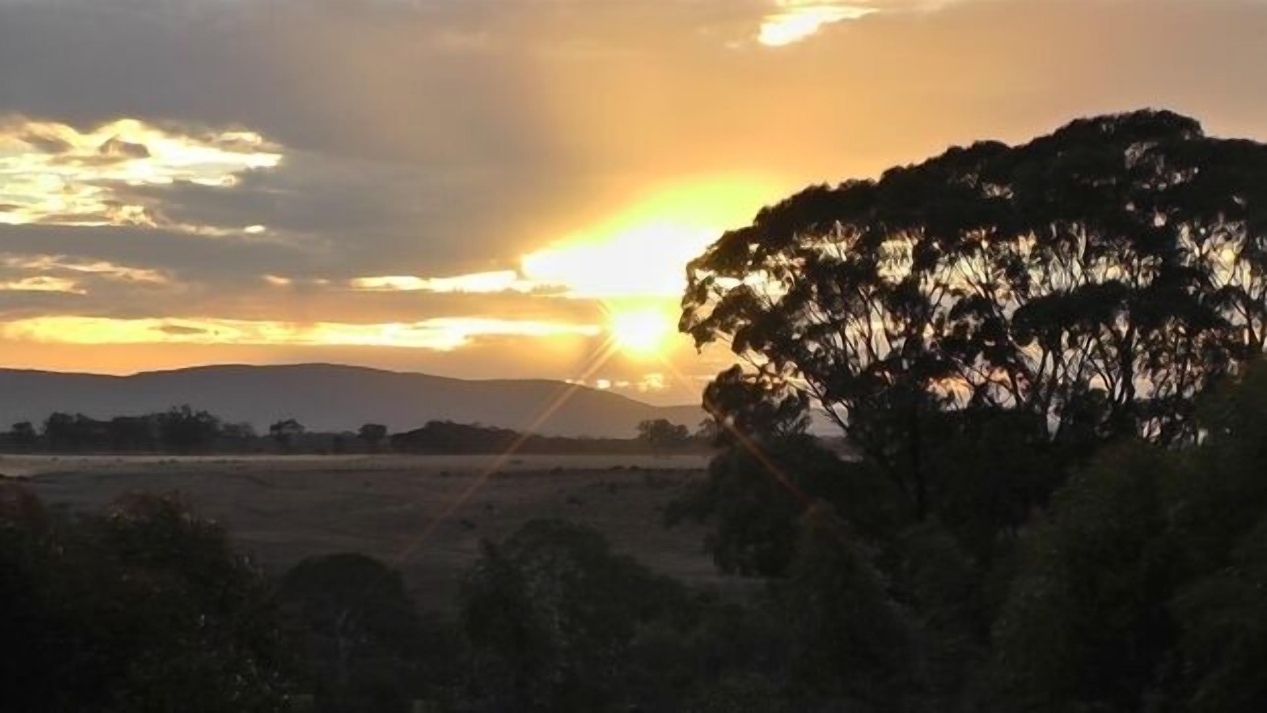 A sunset over a landscape with trees and distant hills.