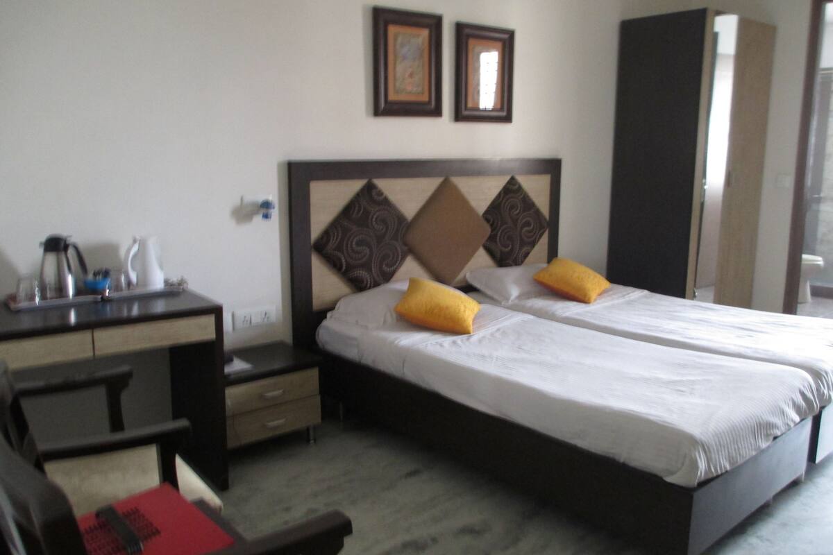 A hotel room with a bed, a desk, and a chair. There are two framed pictures on the wall.