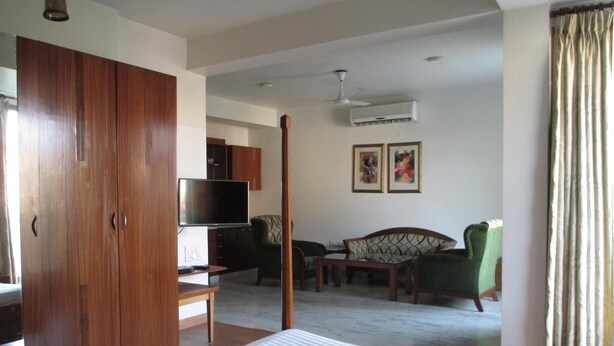 A hotel room with a bed, a TV, a desk, and a chair. There is a wardrobe and an air conditioning unit on the wall. - East End Retreat (New Delhi)
