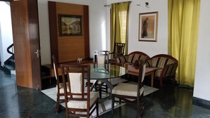 A dining area with a glass-top table surrounded by wooden chairs with cushioned seats. - East End Retreat (New Delhi)