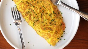A plate with an omelette garnished with chives, accompanied by a fork and a knife on a white plate. - East End Retreat (New Delhi)