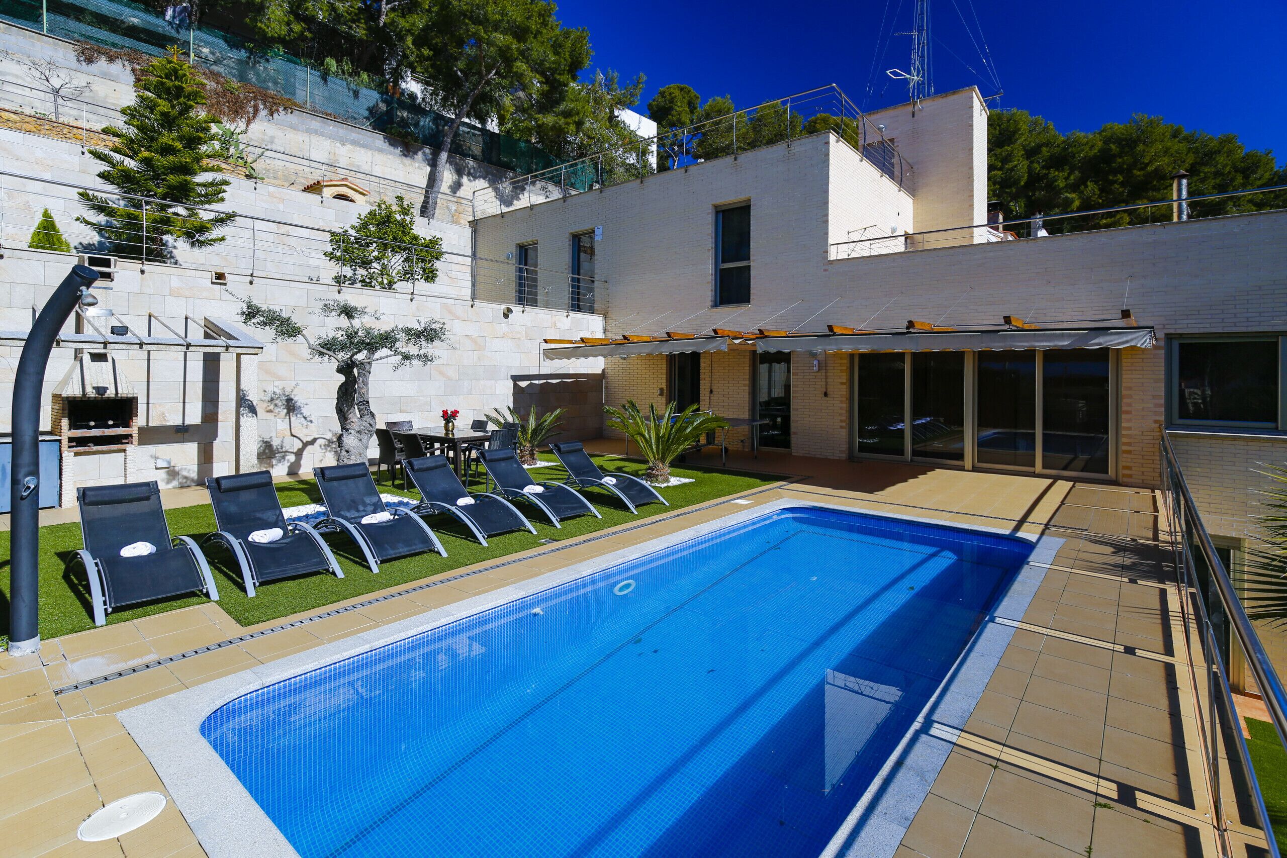 Une piscine avec des chaises longues, un espace patio et un bâtiment doté d’un toit plat et de grandes fenêtres.