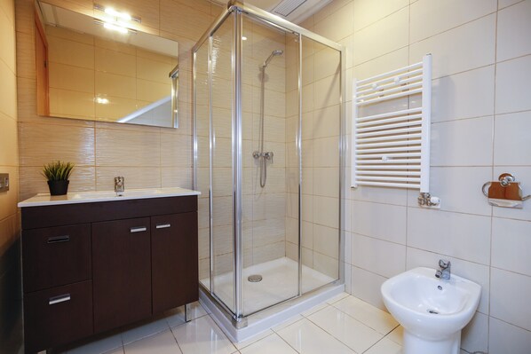 A modern bathroom with a glass-enclosed shower, a white sink, and a bidet.