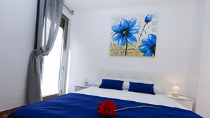 Une chambre à coucher avec un lit, une table de chevet, une lampe et un tableau représentant des fleurs bleues accroché au mur.