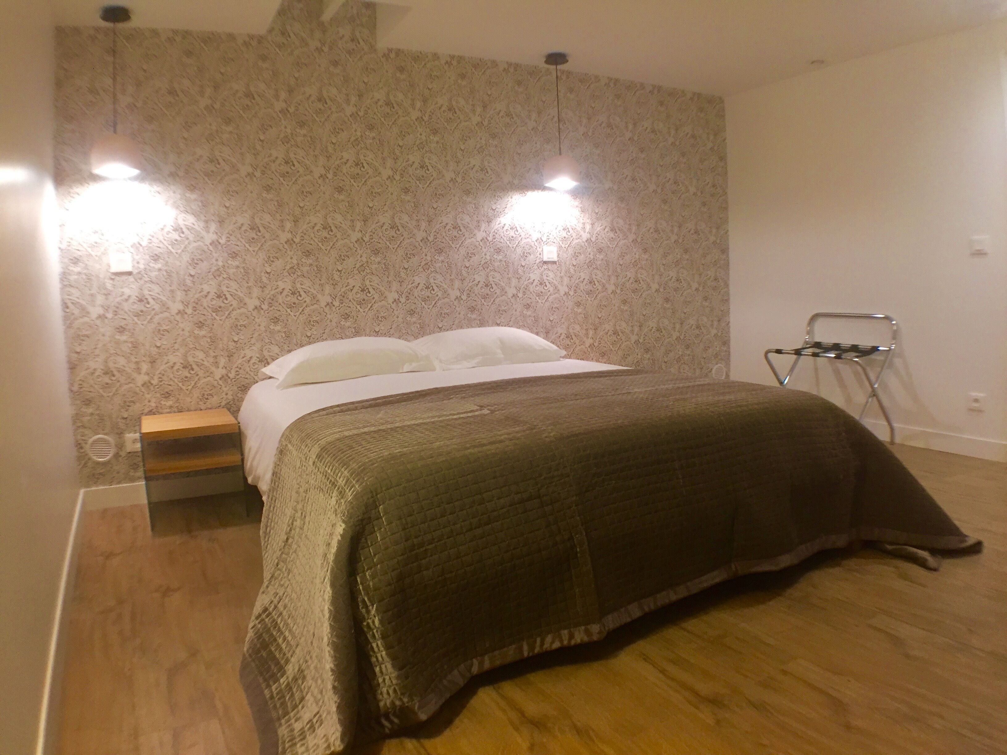 A bedroom with a bed, two wall-mounted lights, a wooden nightstand, and a metal chair.
