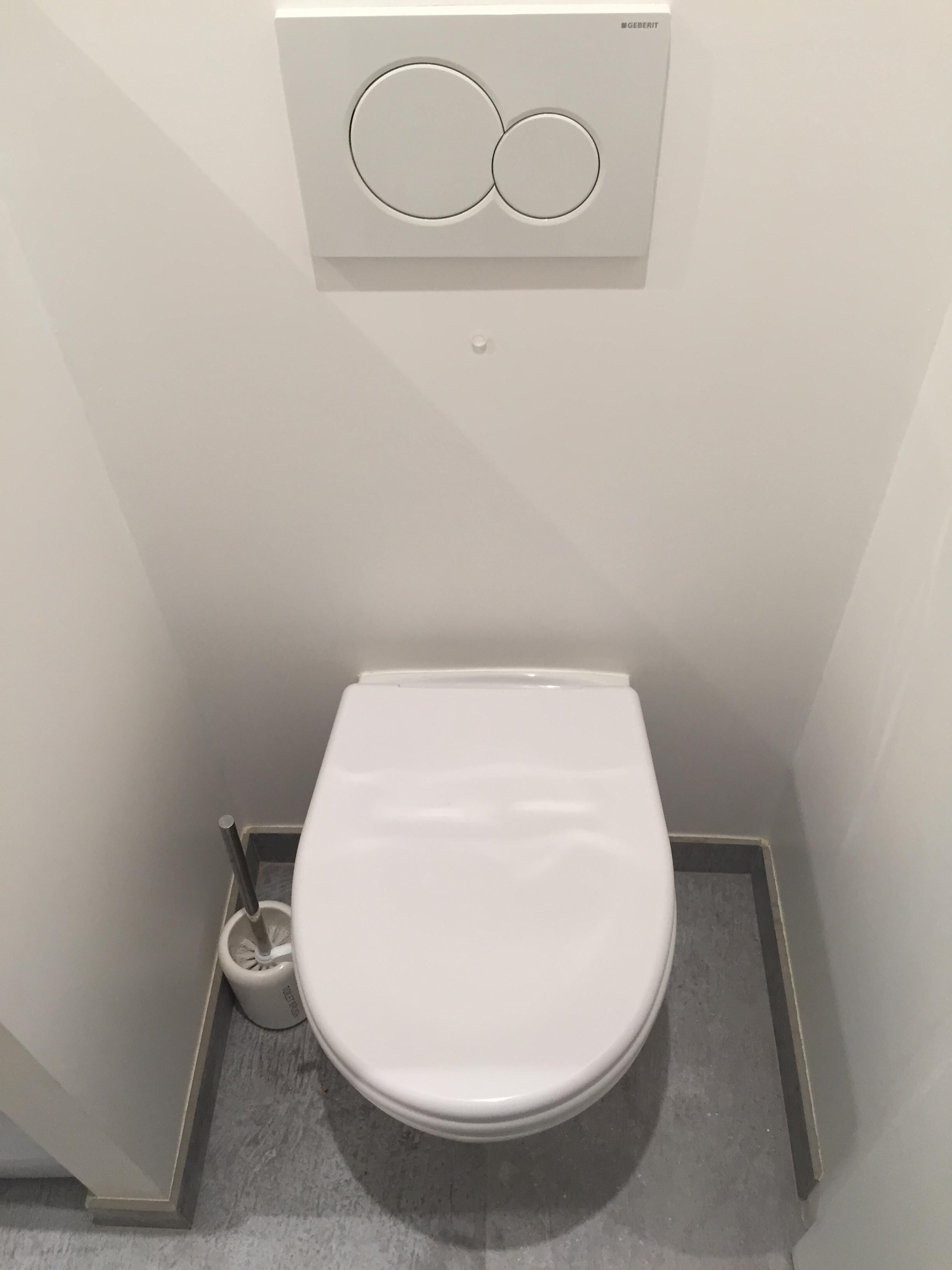 Uma casa de banho moderna com um sistema de descarga embutido na parede e uma escova de sanita.