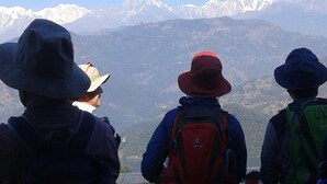 Three people with backpacks and hats, overlooking a mountainous landscape with snow-capped peaks. - Ram Homestay (Lekhnath)