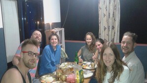 A group of people sitting around a table with various dishes, a bottle, and a candle. - Ram Homestay (Lekhnath)