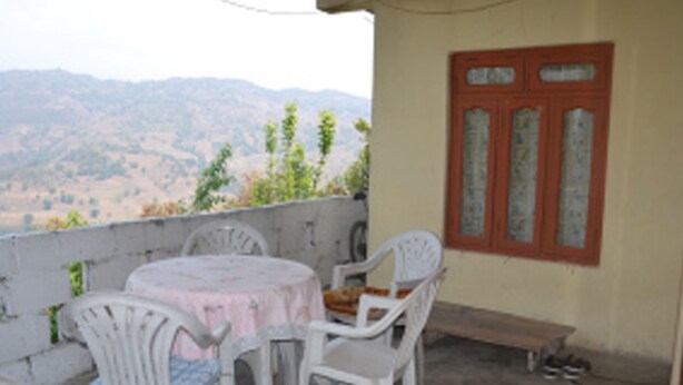 A balcony with a table and chairs, a wooden bench, and a door with glass panels. - Ram Homestay (Lekhnath)