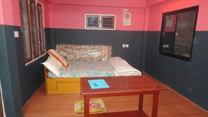 A room with a bed, a small wooden table, a window, and a door. - Ram Homestay (Lekhnath)