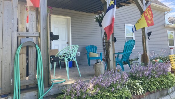 Une véranda en bois dotée d’un espace abrité, de chaises d’extérieur et d’un mât sur lequel sont hissés plusieurs drapeaux.