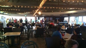 Un restaurant avec des tables et des chaises, une scène pour des concerts, et une vue sur l’extérieur.