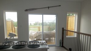 Une cuisine dotée d’un grand îlot central, d’une table à manger et d’une porte-fenêtre coulissante donnant sur une cour arrière avec un patio couvert et une clôture en bois.