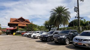 A row of parked cars in front of a building with a red roof and a signboard. - Hugphaeng Garden (Ban Phaeng)