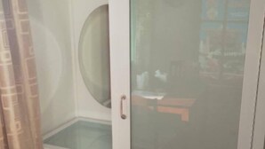 A room with a white door, a glass shower enclosure, and a small table with a chair. - Hugphaeng Garden (Ban Phaeng)