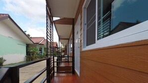 A corridor with wooden flooring, a black railing, and a view of neighboring houses. - Hugphaeng Garden (Ban Phaeng)
