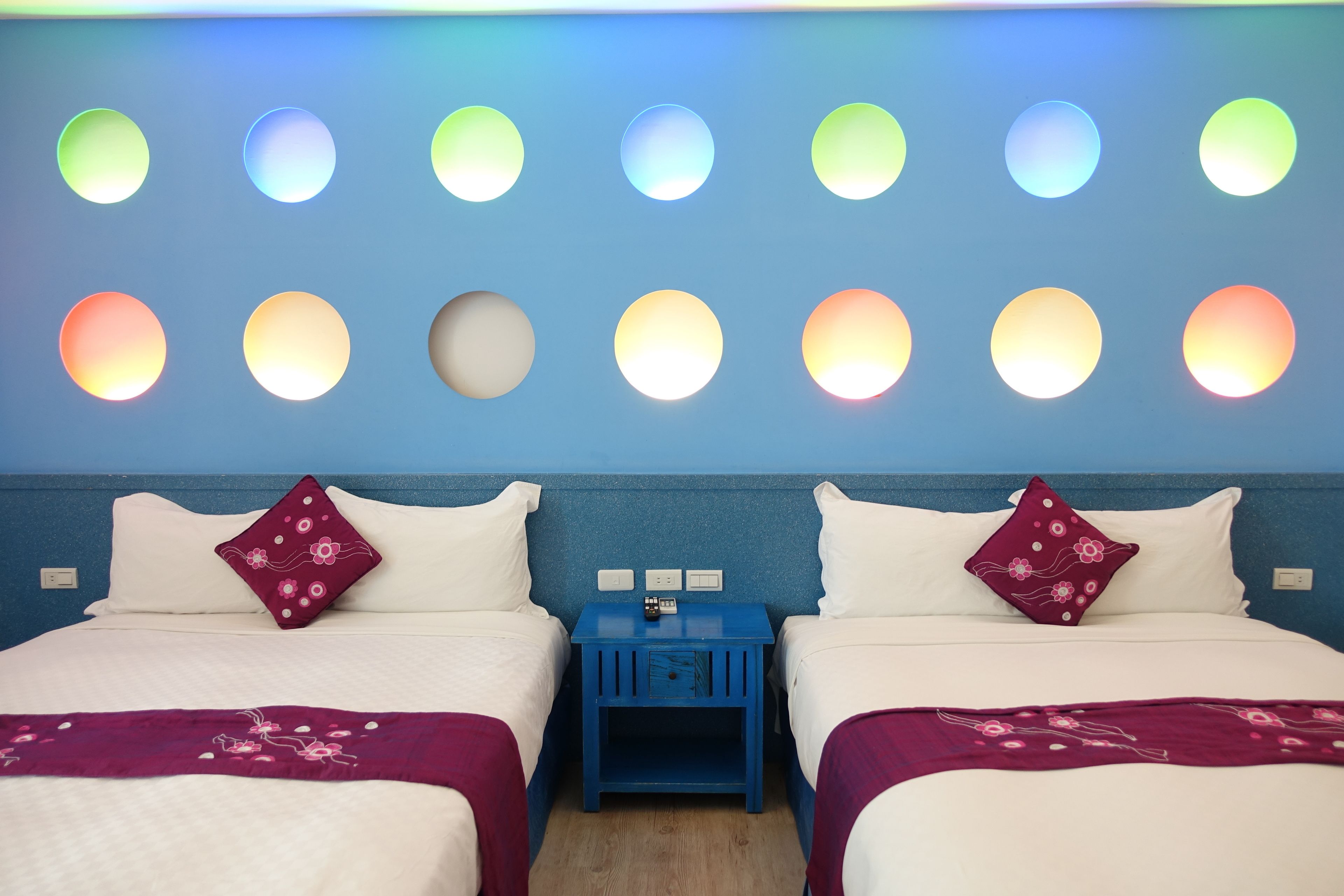 Una habitación de hotel con dos camas, una mesita de noche y una pared con lámparas circulares.