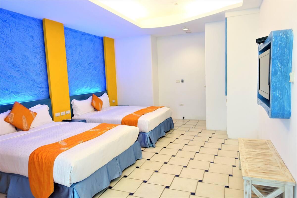Ein Hotelzimmer mit zwei Betten, einem kleinen Holztisch und einem großen Fenster.