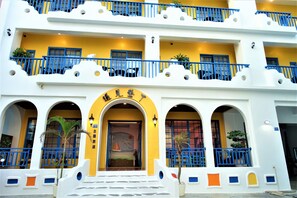 A hotel with a yellow facade, blue balconies, and a central entrance with a sign. - Meet Kenting (Hengchun)