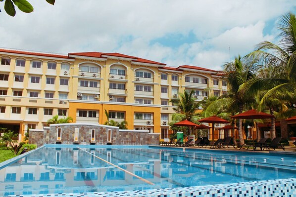 A hotel with a swimming pool, palm trees, and a red-roofed building.