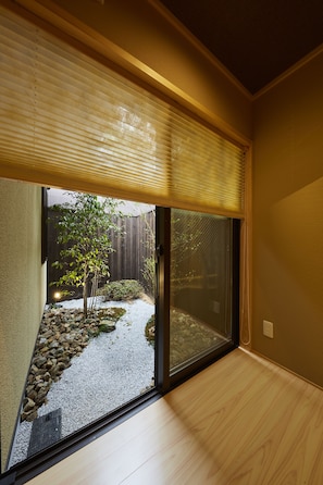 A room with a sliding glass door leading to a garden with a tree and gravel path.