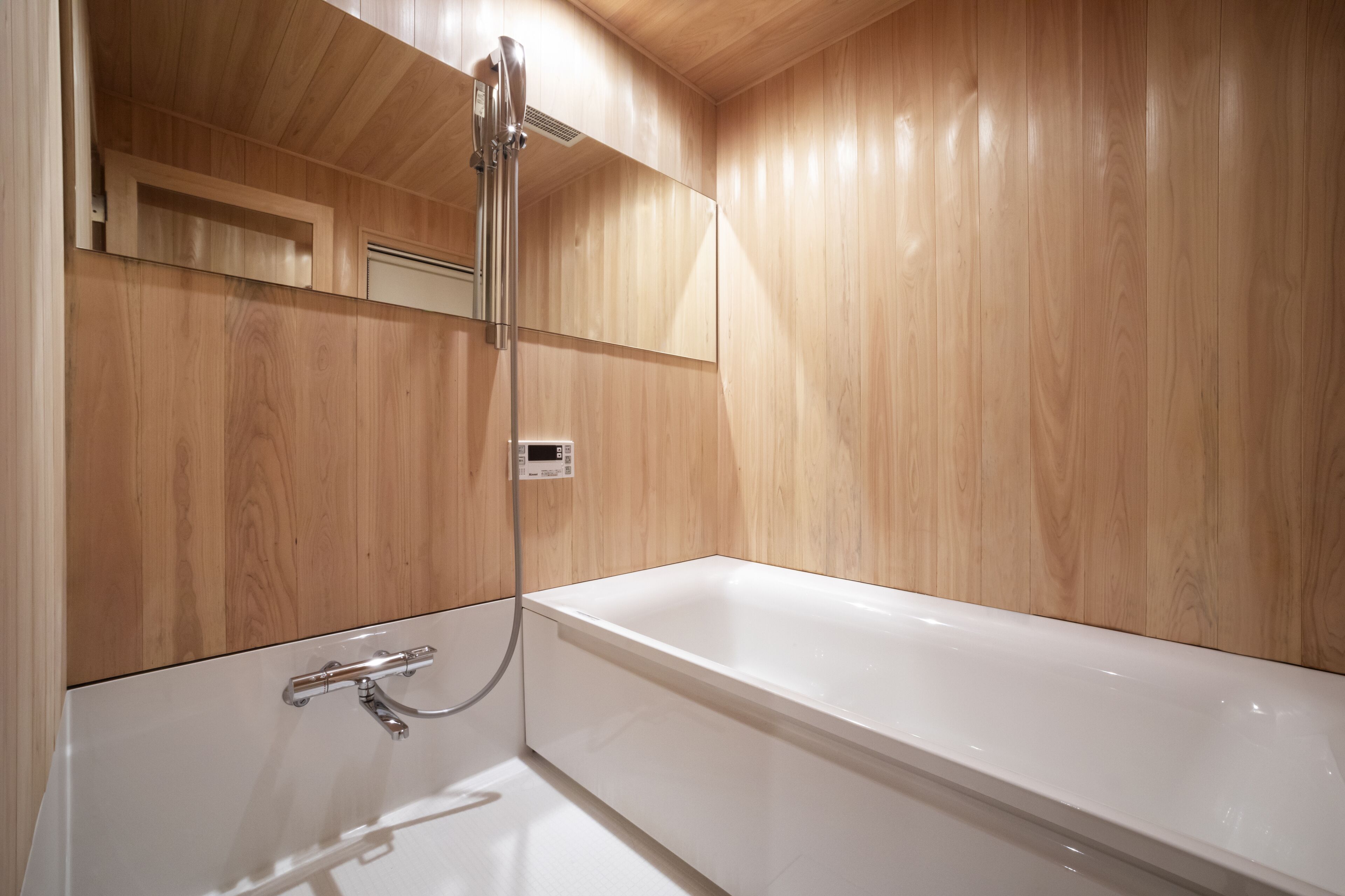 A modern bathroom with a wooden interior, a white bathtub, and a handheld showerhead.